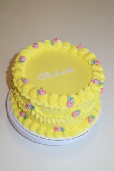 Gul kage med små rosa blomster og dekorativ frosting