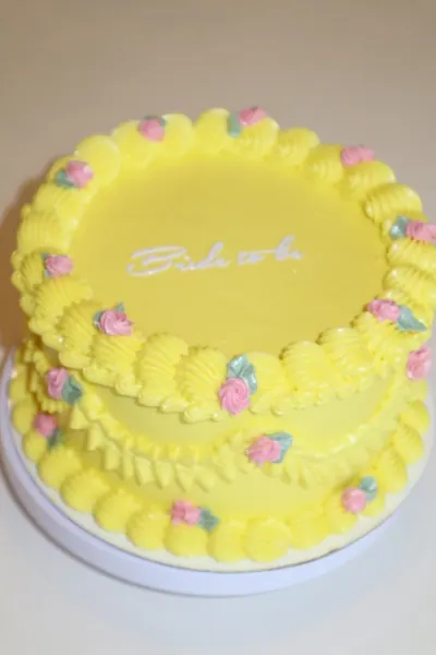 Gul kage med små rosa blomster og dekorativ frosting