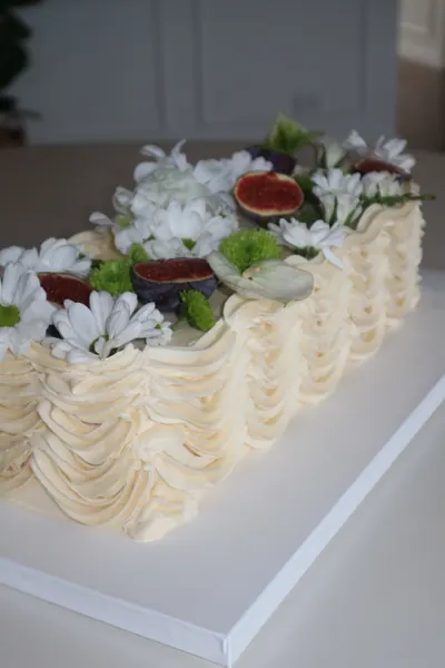 Lang lys kage med blomster, grønne blade og røde bær