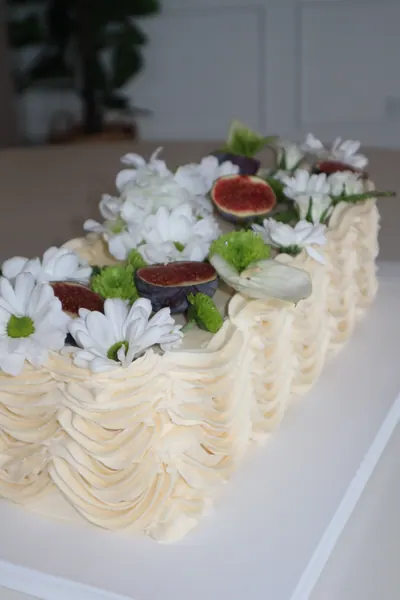 Lang lys kage med blomster, grønne blade og røde bær