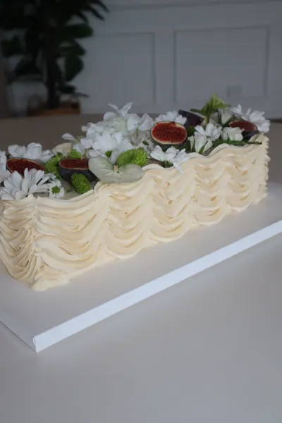 Lang lys kage med blomster, grønne blade og røde bær