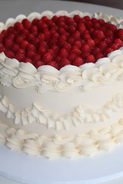 Hvid hjertekage med røde bær og dekorativ frosting