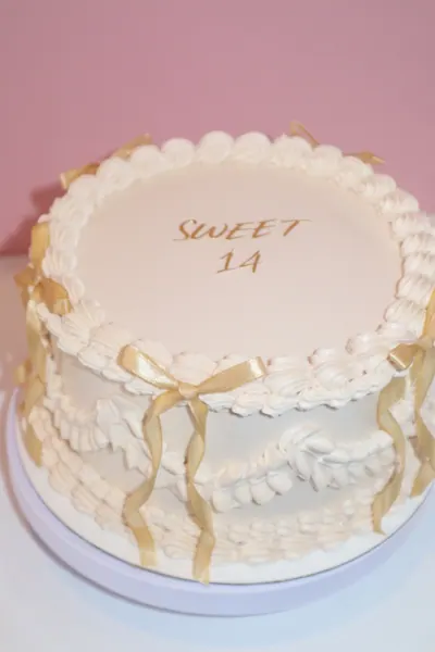 Lys rund kage med gyldne detaljer og dekorativ frosting