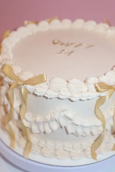 Lys rund kage med gyldne detaljer og dekorativ frosting