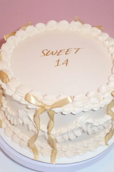 Lys rund kage med gyldne detaljer og dekorativ frosting
