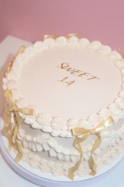 Lys rund kage med gyldne detaljer og dekorativ frosting