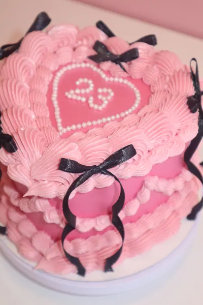 Pink hjertekage med sorte sløjfer og fine detaljer i frosting